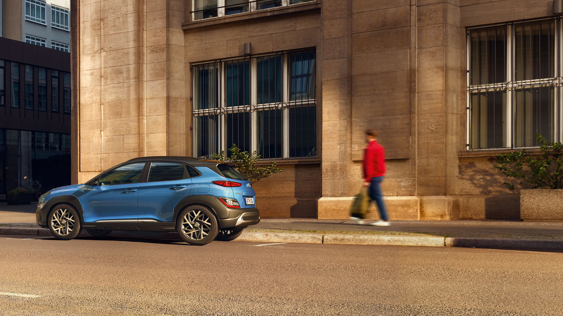Pohled z boku na nové SUV Hyundai KONA Hybrid, zaparkované na ulici ve městě.